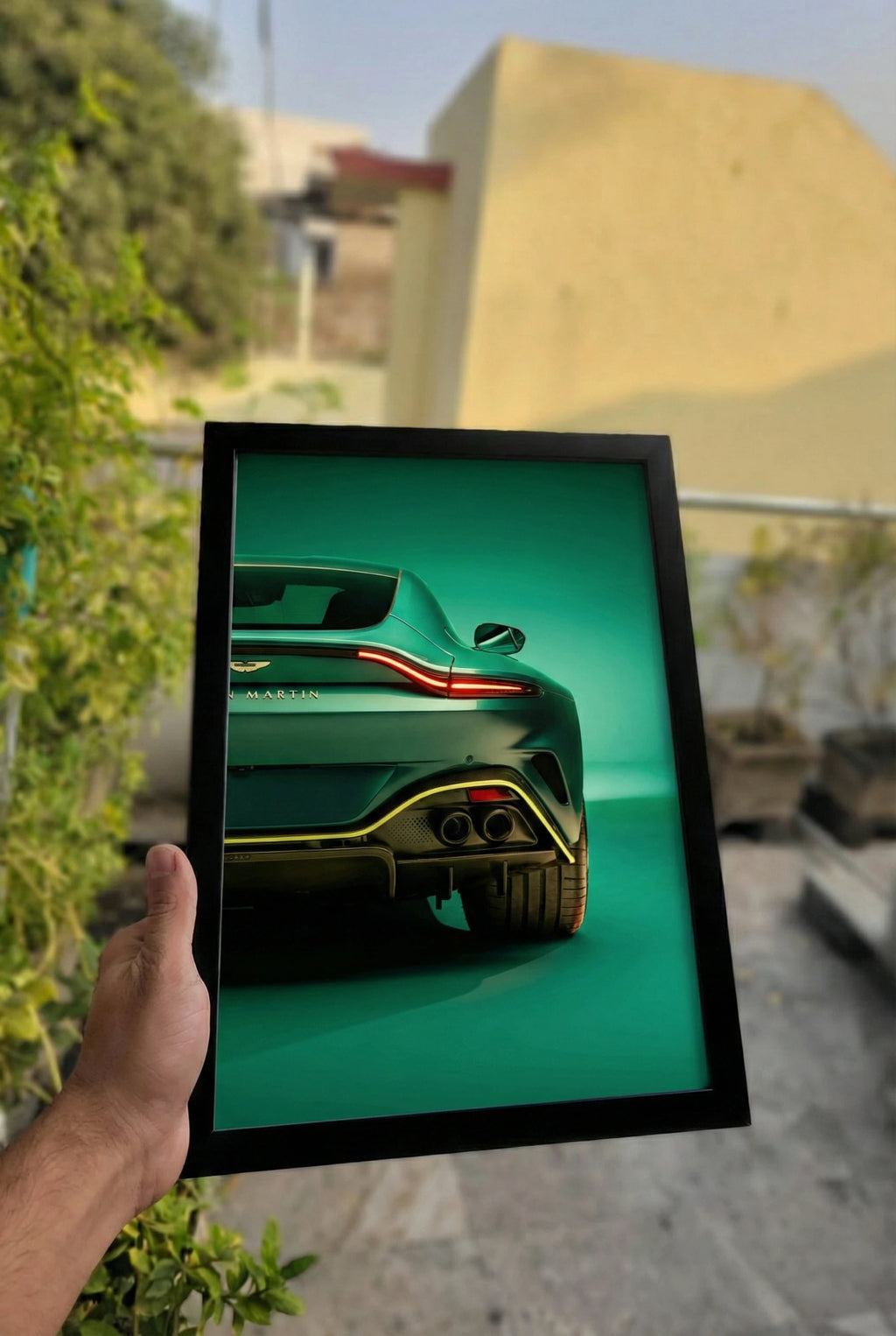 Framed picture of a green car held by a hand outdoors.